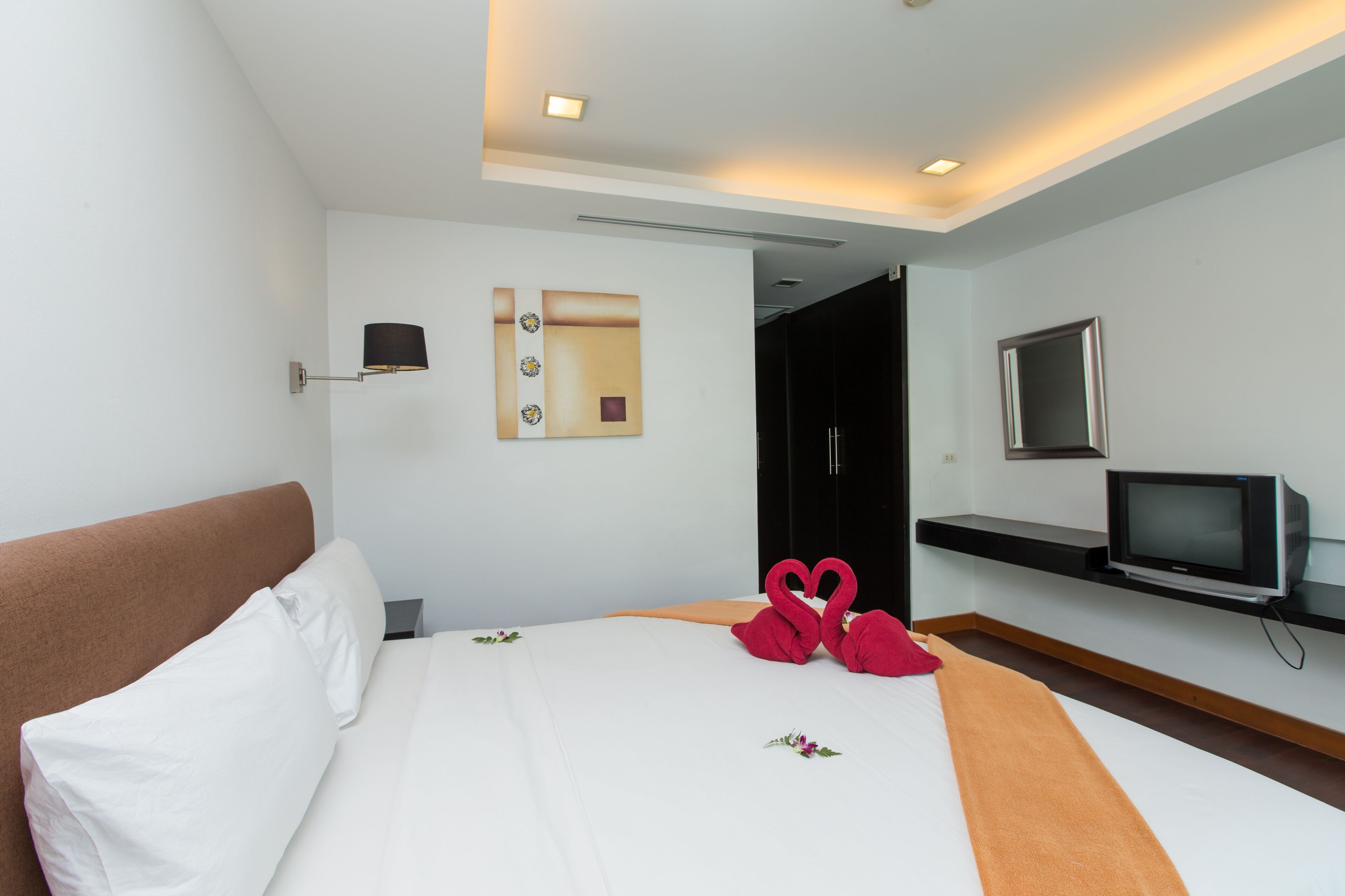 A hotel room with a bed, a TV, a mirror, and a wall-mounted shelf.