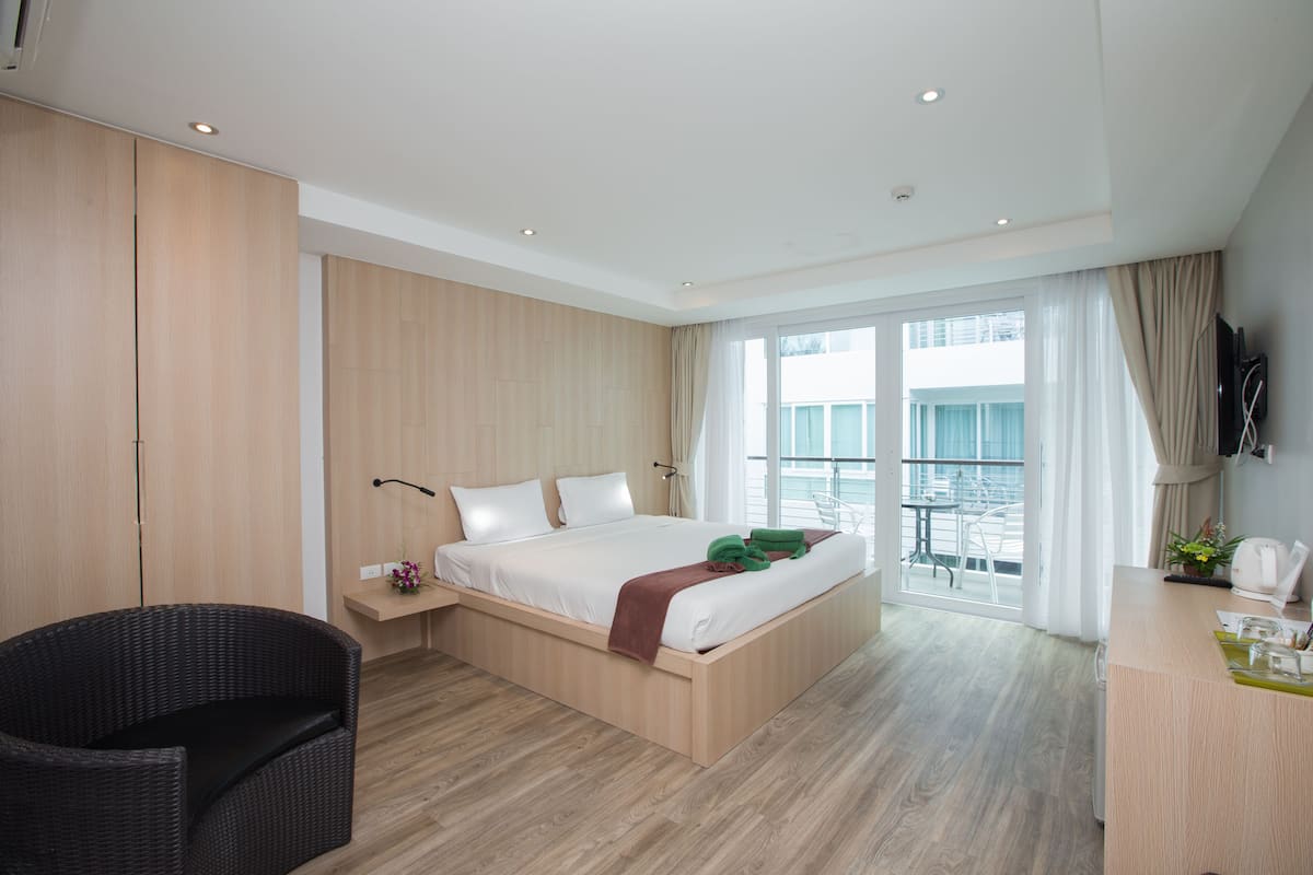 A modern hotel room with a large bed, a desk, and a balcony with a view.