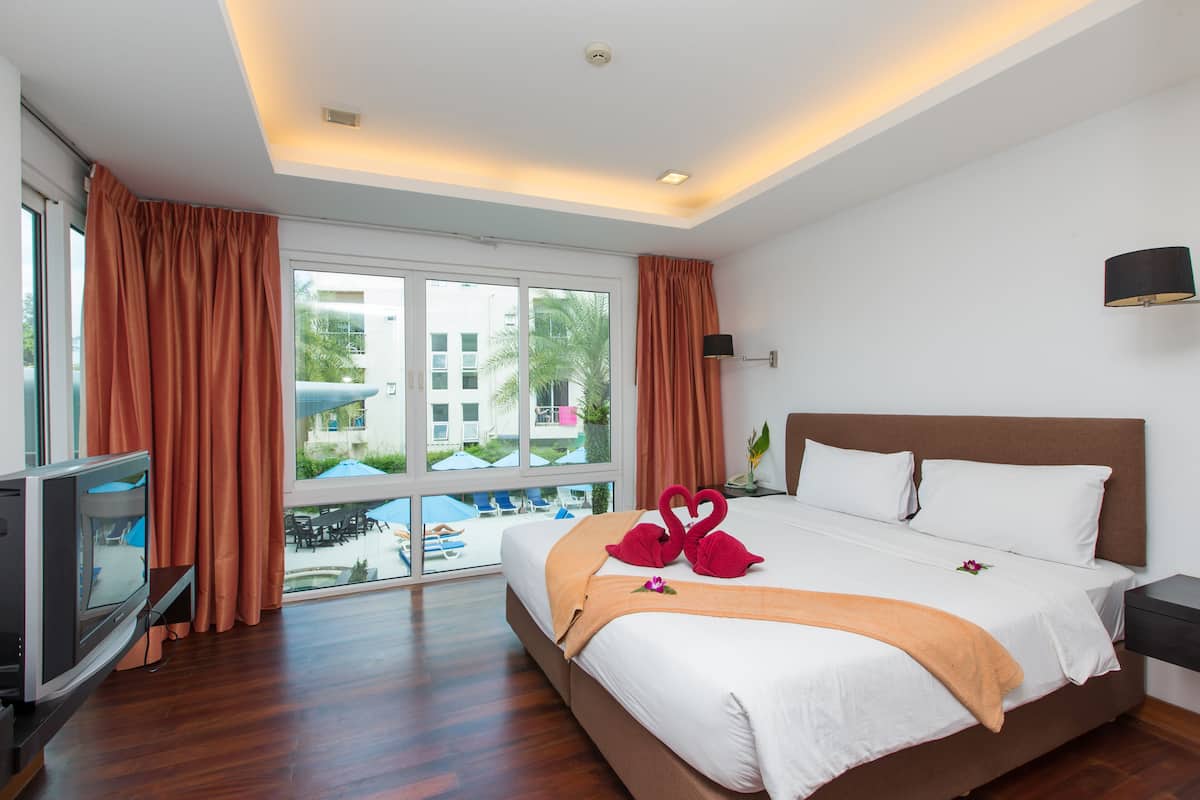 A hotel room with a large bed, a television, and a view of the pool and buildings outside.