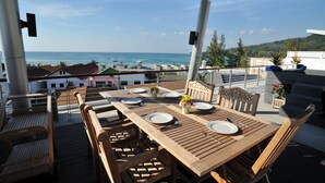 A wooden deck with a table set for dining, overlooking a beach and ocean. - The Palms Kamala Beach (Kamala)