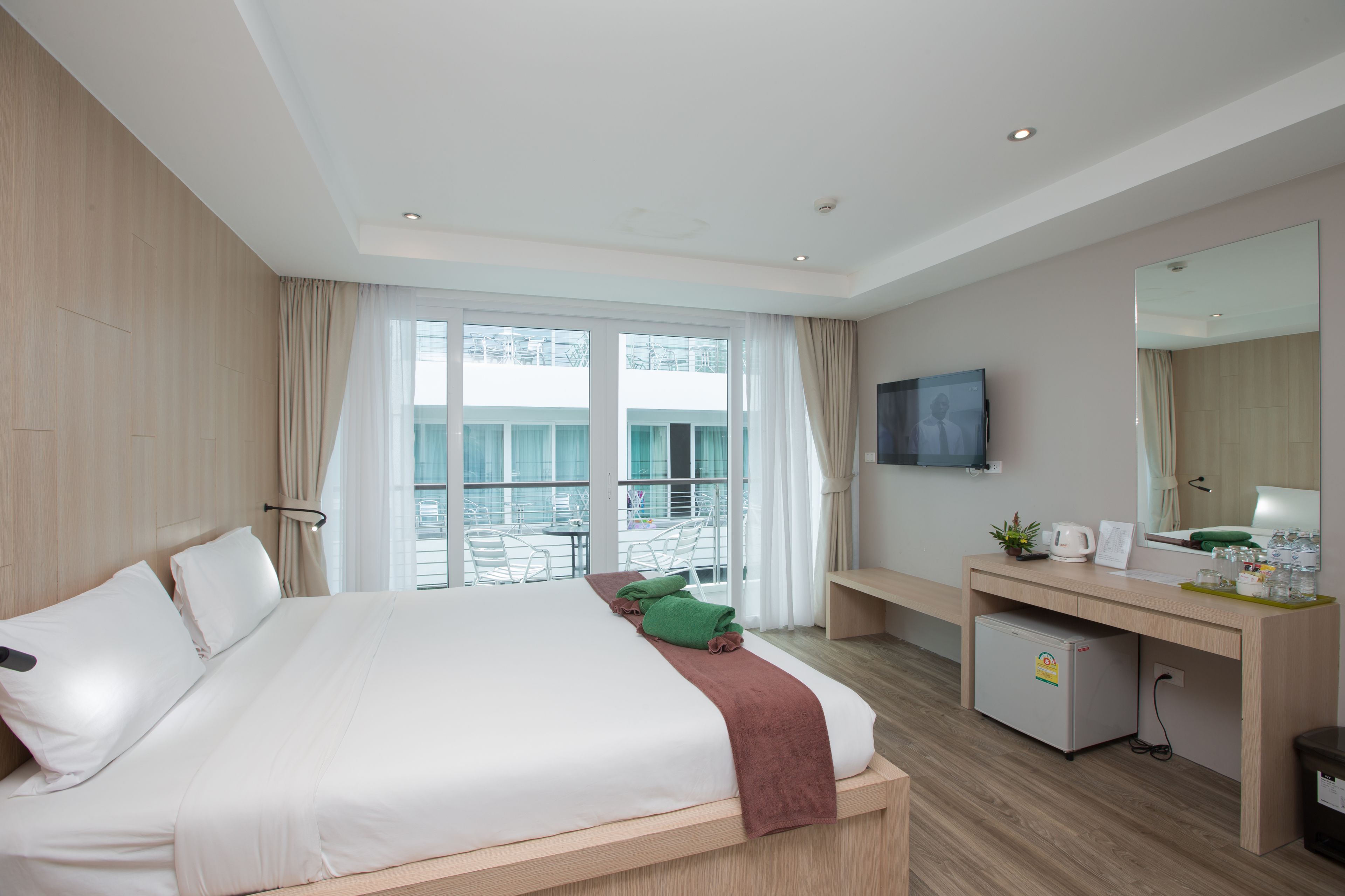 A hotel room with a large bed, a desk, a small fridge, and a balcony with a view.