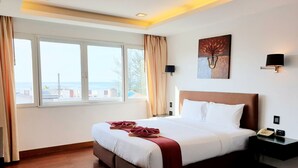 A hotel room with a large bed, a bedside table with a phone, a wall-mounted lamp, and a painting. - The Palms Kamala Beach (Kamala)