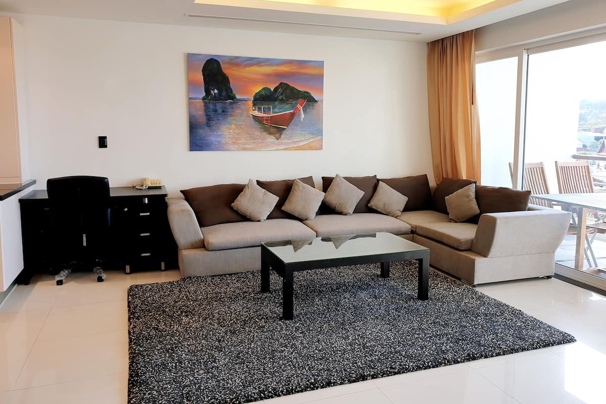 A modern living room with a sectional sofa, a coffee table, and a painting of a sunset over water.