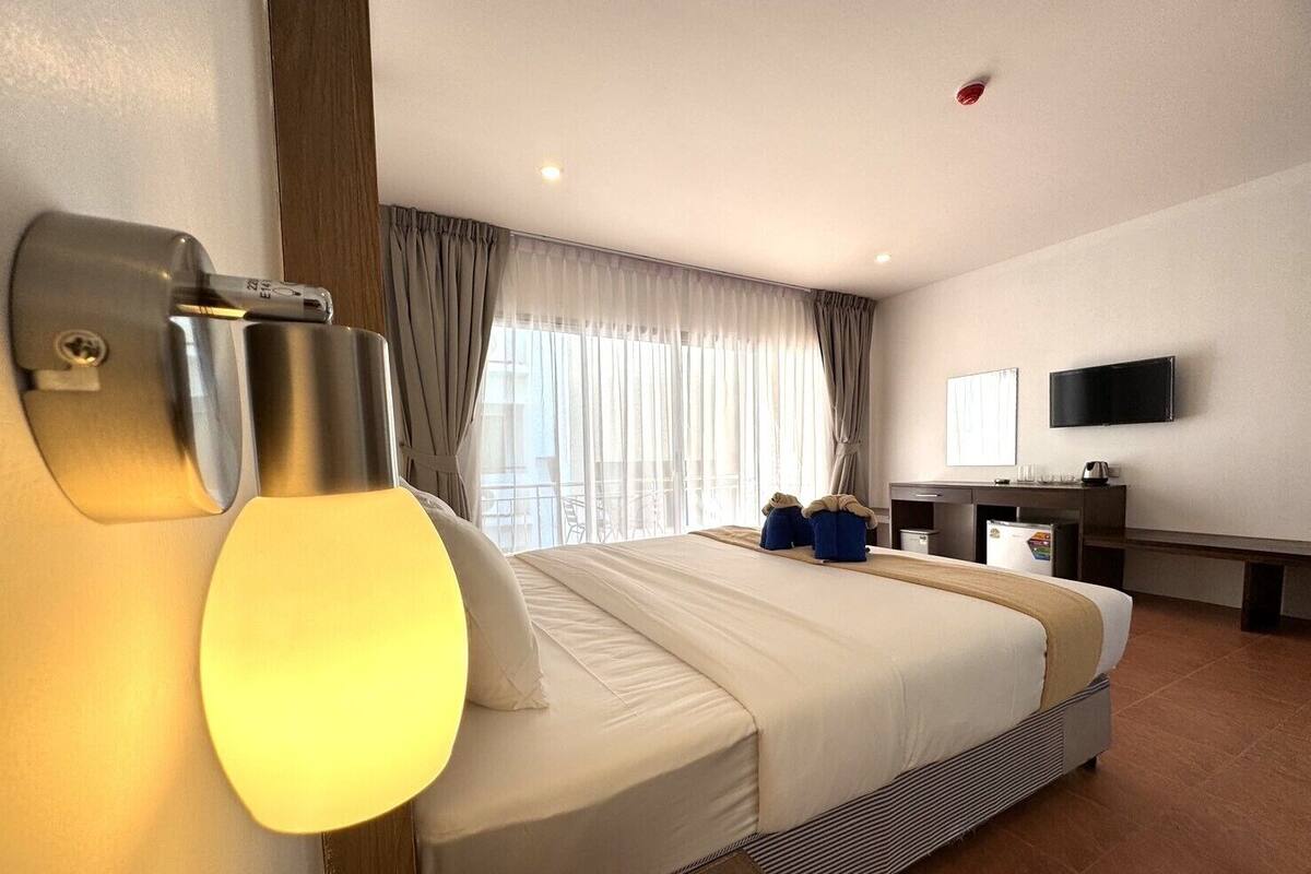 A hotel room with a bed, a desk, a TV, and a window with curtains.