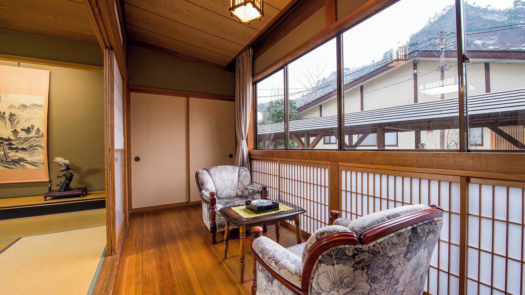 Una habitación japonesa tradicional con suelo de tatami, techo de madera bajo y vistas a un edificio tradicional a través de un amplio ventanal.