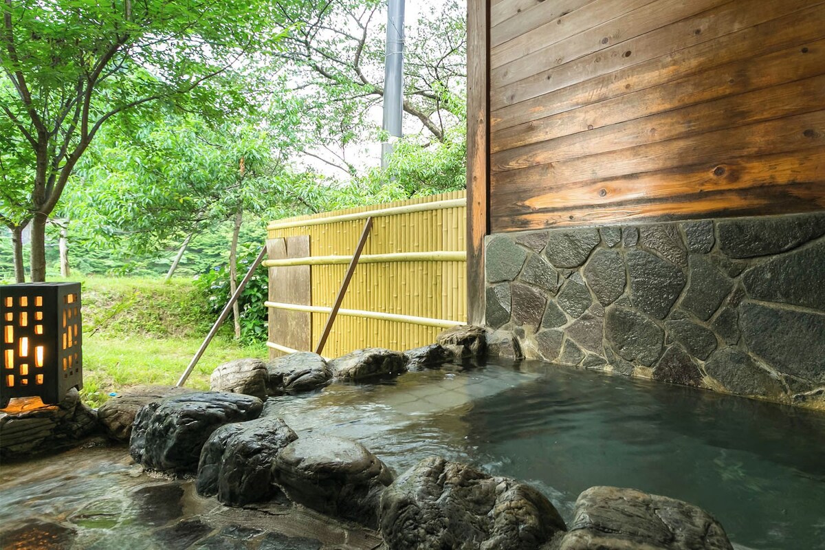 Un onsen japonés tradicional con un edificio de madera, pared de piedra y valla de bambú.