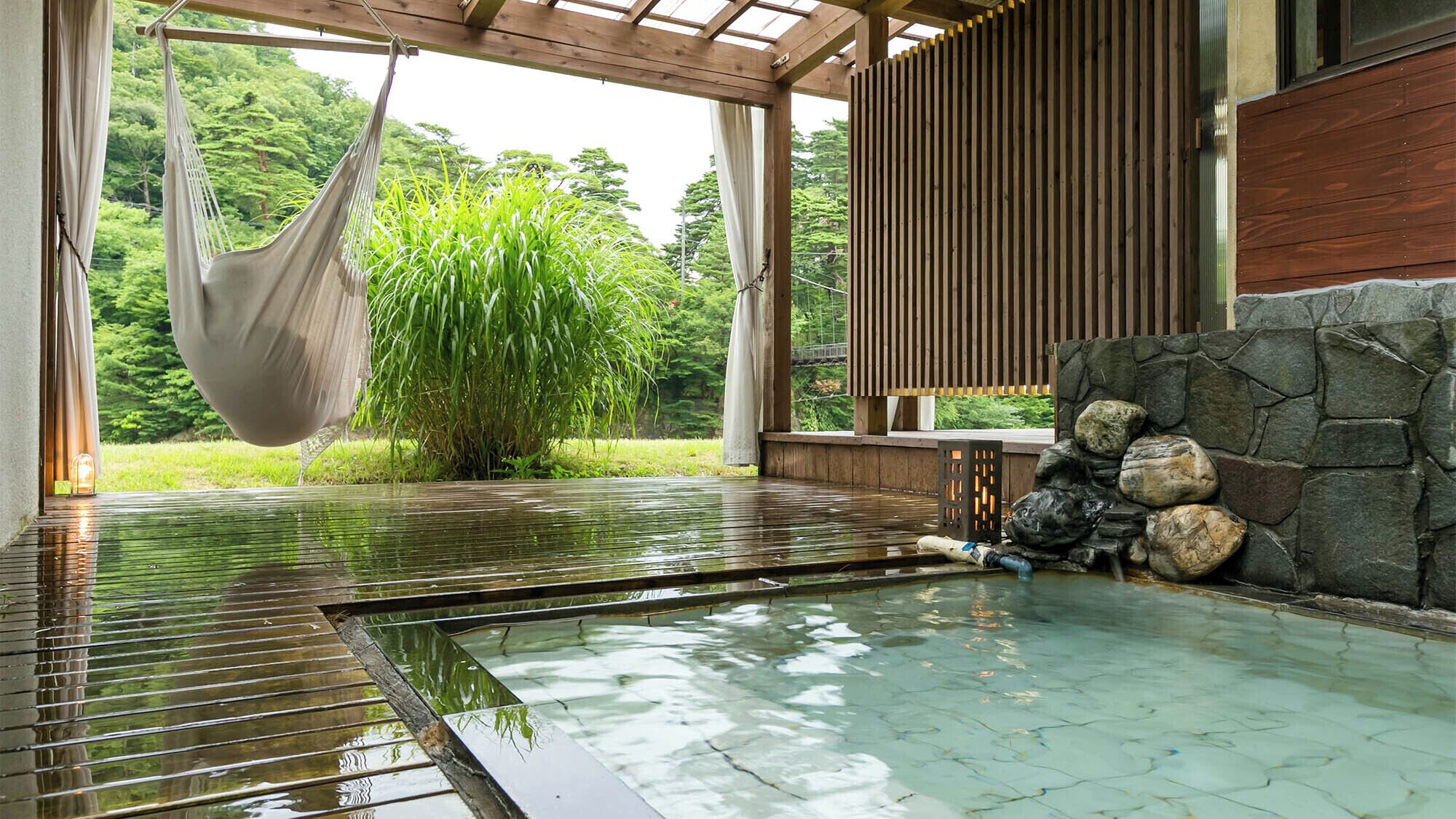 Un área de piscina interior tranquila con una hamaca, pared de piedra y vigas de madera.