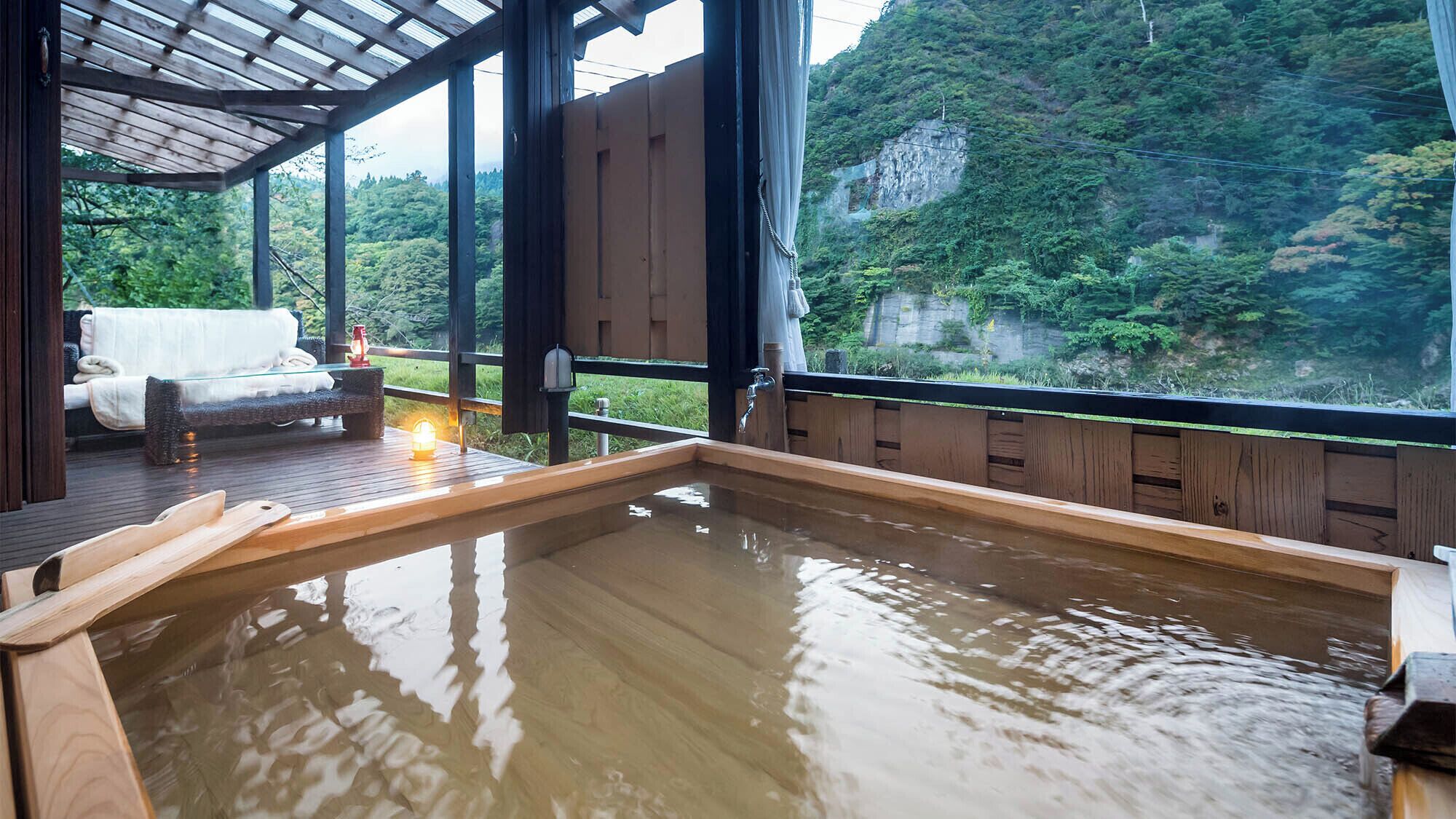 Un baño de aguas termales con una terraza de madera, un banco y vistas a una ladera boscosa.