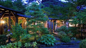 A traditional Japanese garden with wooden structures, lush greenery, and a stone pathway. - Takanosu Onsen Takanosukan (Sekikawa)