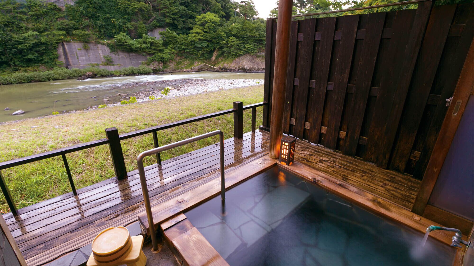 Una terraza de madera con un jacuzzi, un banco de madera y vistas a un río.