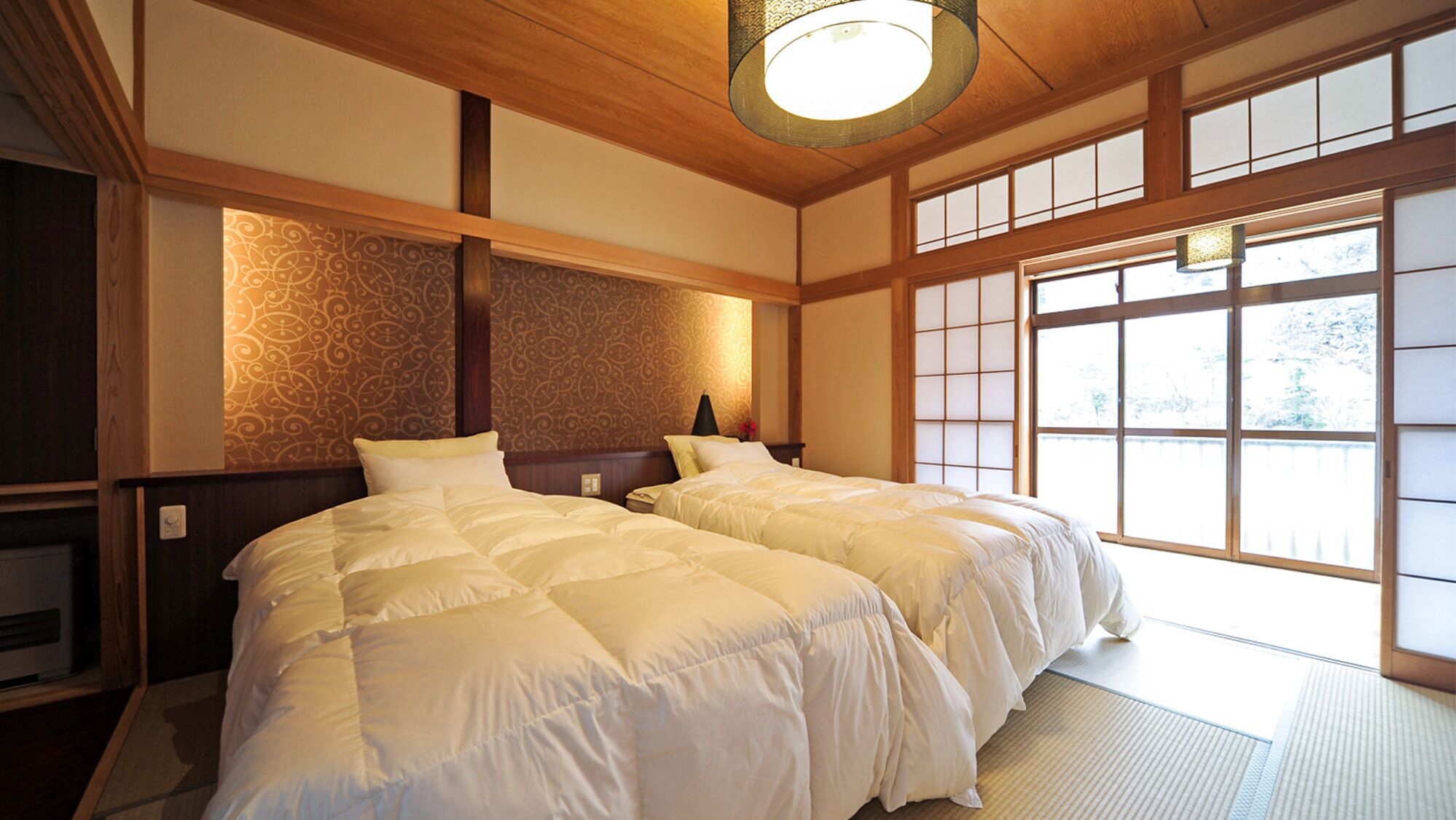 Una habitación tradicional japonesa con suelo de tatami, un ventanal con puertas shoji y una lámpara colgante en el techo.