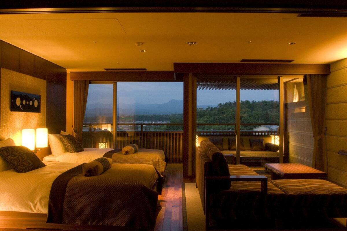 Ein Hotelzimmer mit einem großen Bett, einem kleineren Bett, einer Couch und einem Tisch. Ein Balkon bietet Blick auf die Berge.