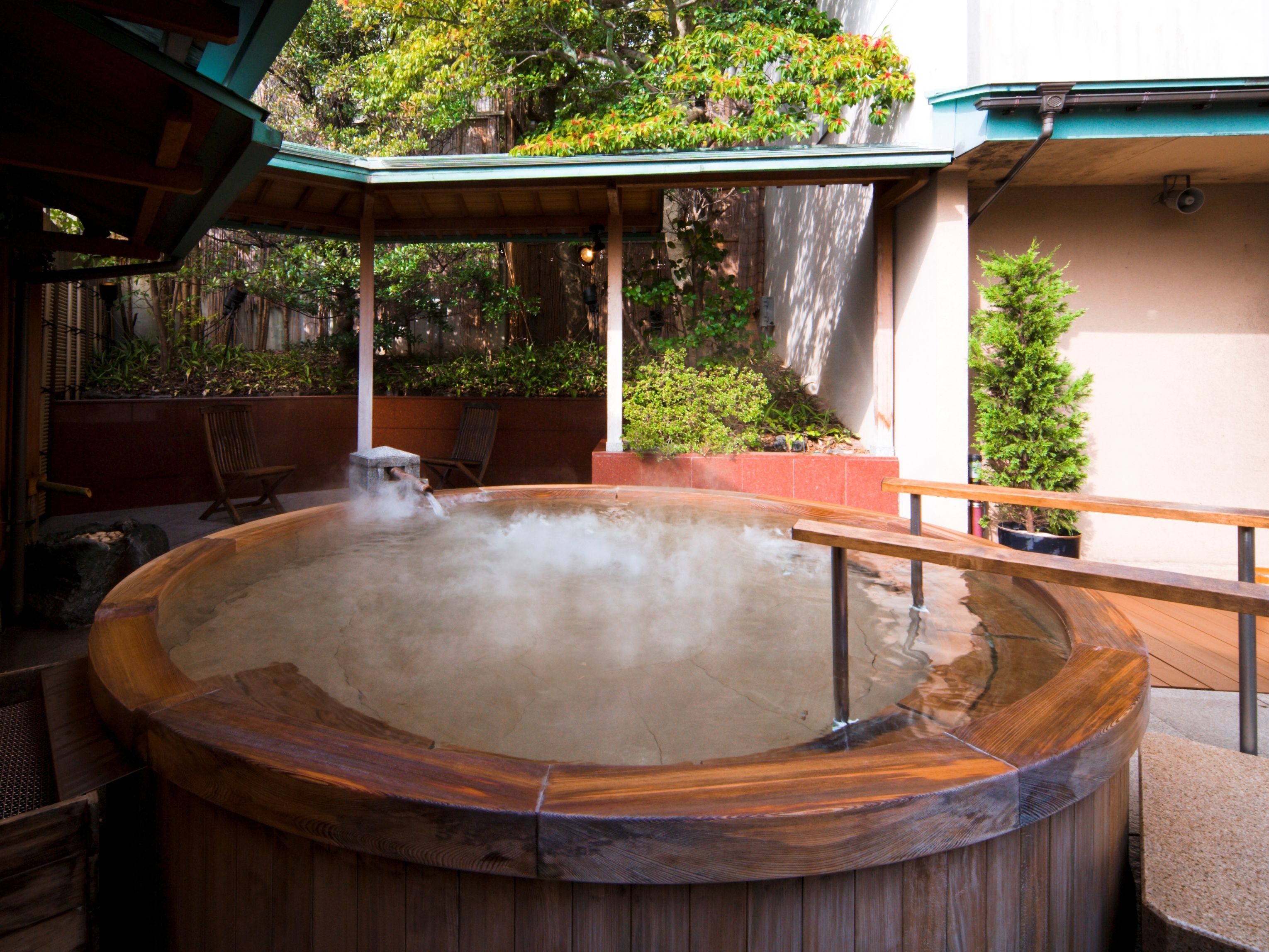 A hot tub with a wooden exterior, surrounded by outdoor furniture and greenery.
