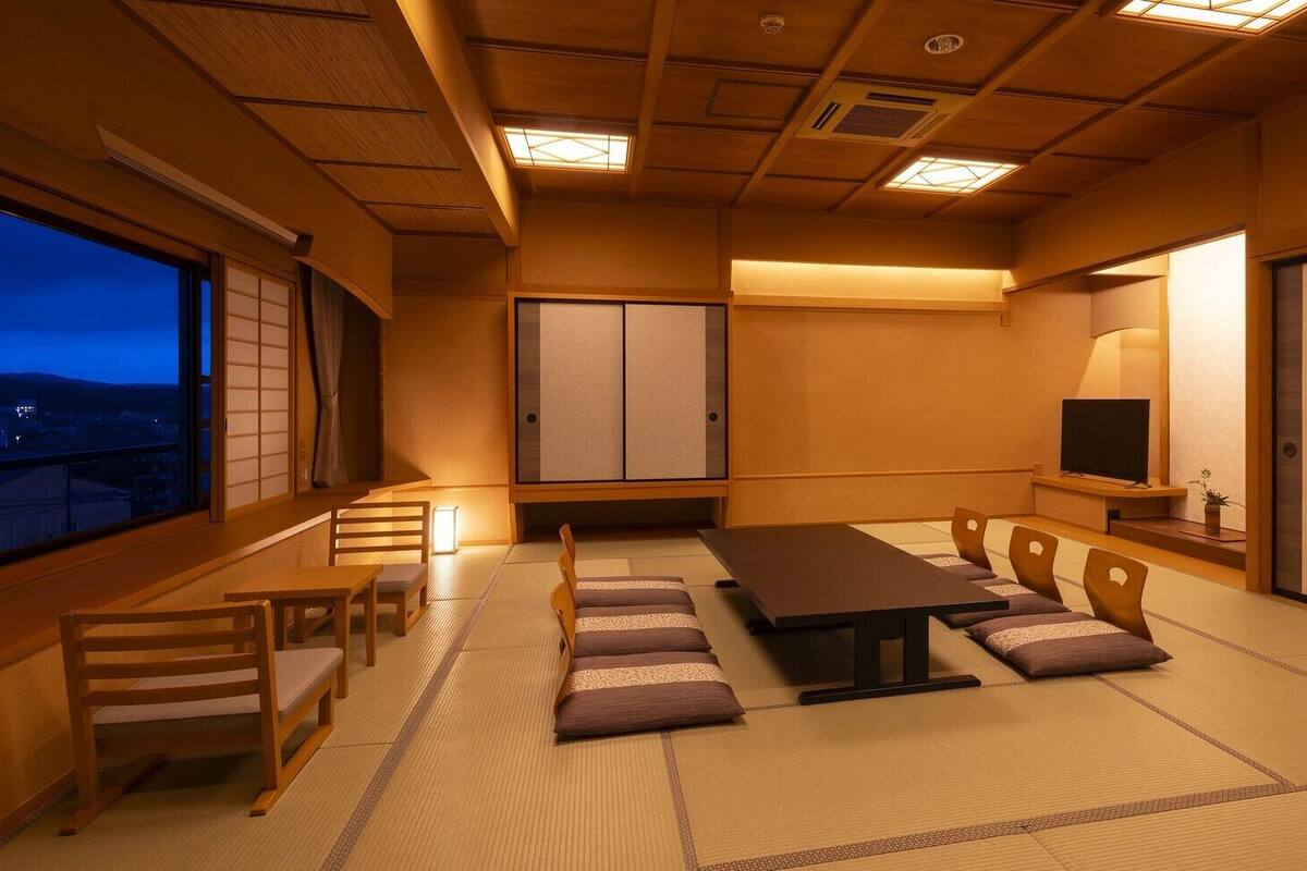 Ein traditioneller japanischer Raum mit Tatami-Böden, einem niedrigen Tisch, Holzsesseln, Schiebetüren und einem Fernseher.