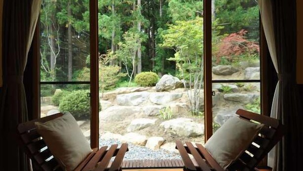 A room with two wooden lounge chairs facing a large sliding glass door leading to a garden with rocks and trees. - All Resort Service Holiday Homes and Cottages to Rent (Inawashiro)