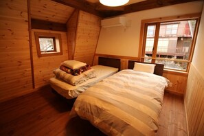 Una habitación acogedora tipo cabaña de madera, con cama, ventana y un tragaluz pequeño.