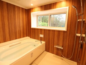 Un baño moderno con pared de madera, una bañera grande, ducha y ventana con vista a árboles.