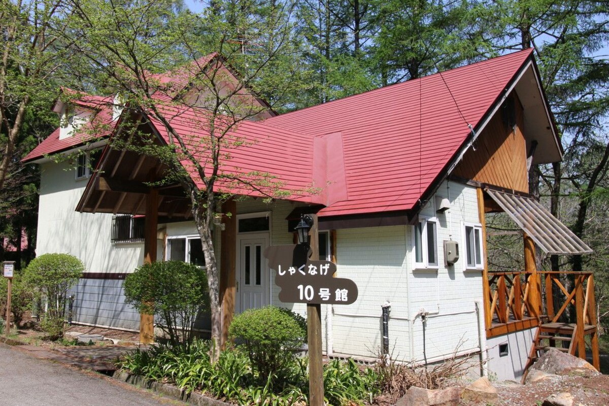 A traditional Japanese house with a red roof, surrounded by trees and a small garden.
