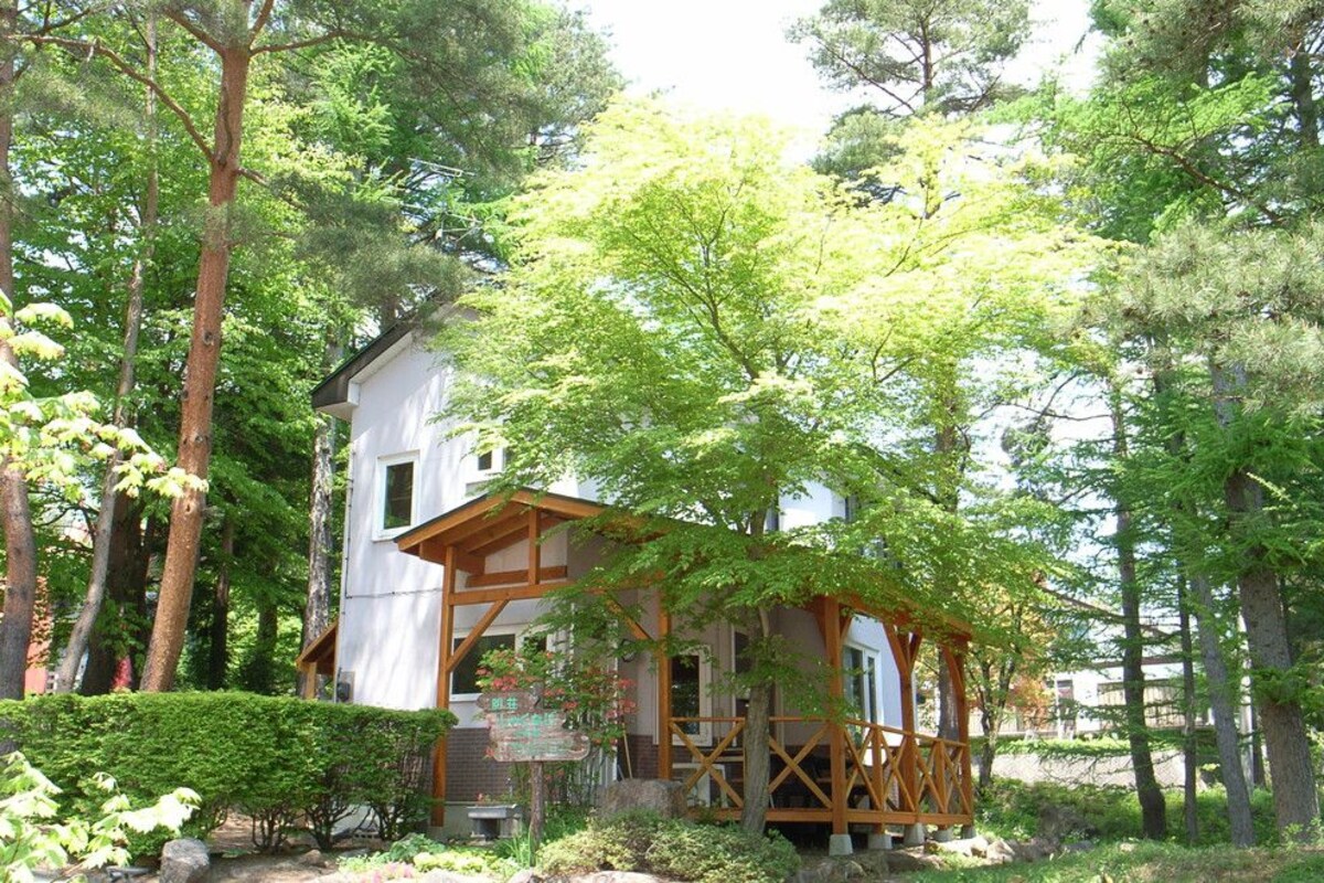 A small wooden cabin with a porch, surrounded by dense forest.