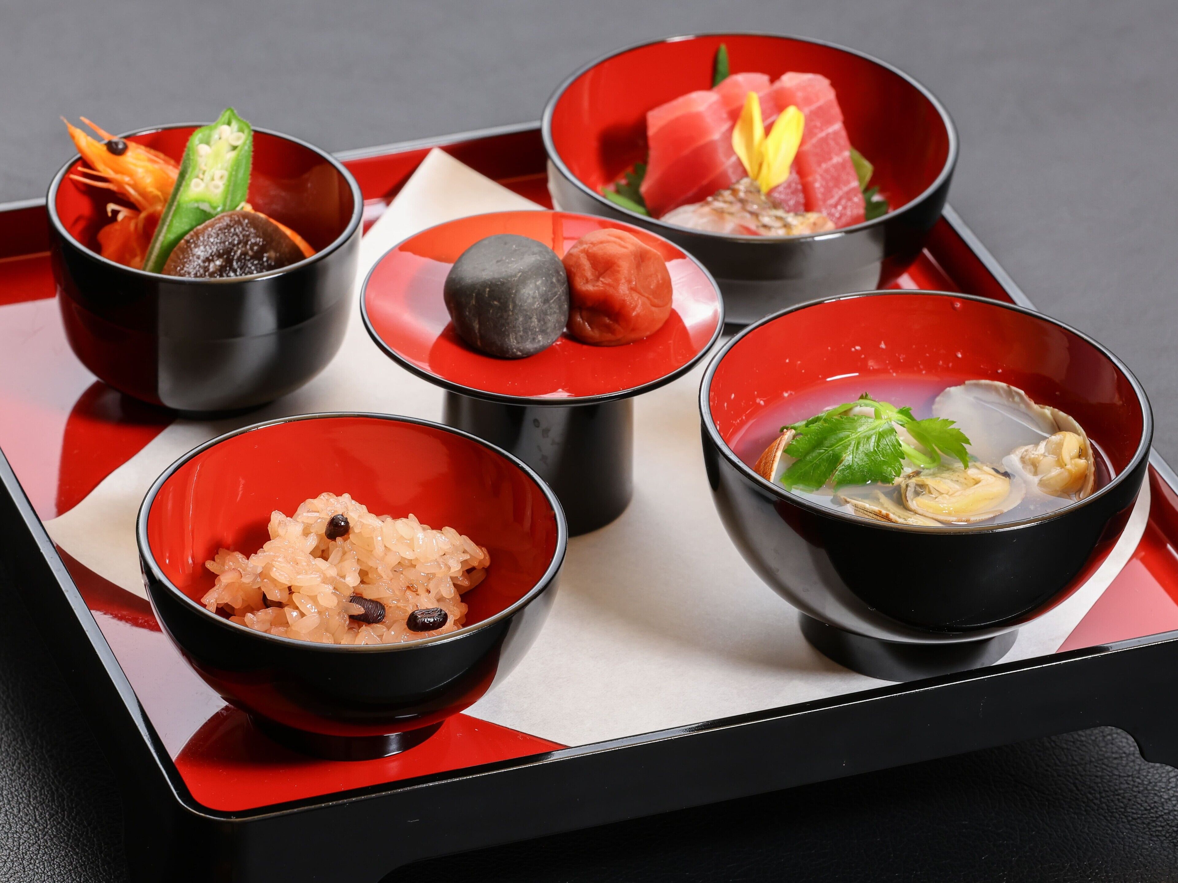 A tray with five black bowls containing various dishes, including sushi and rice.