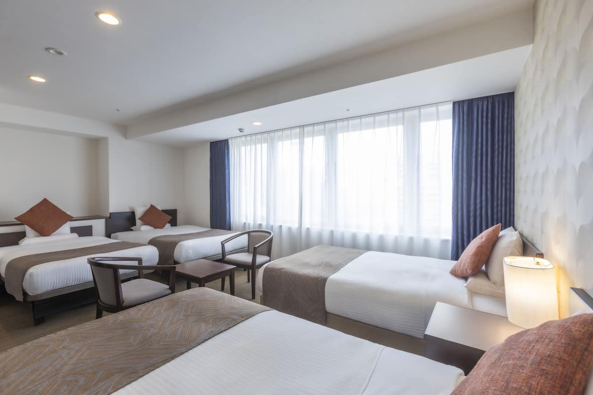 A hotel room with two beds, a desk, a chair, and a lamp.
