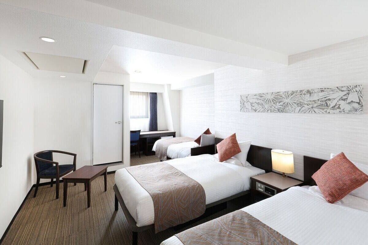 A hotel room with two beds, a desk, a chair, and a large window.