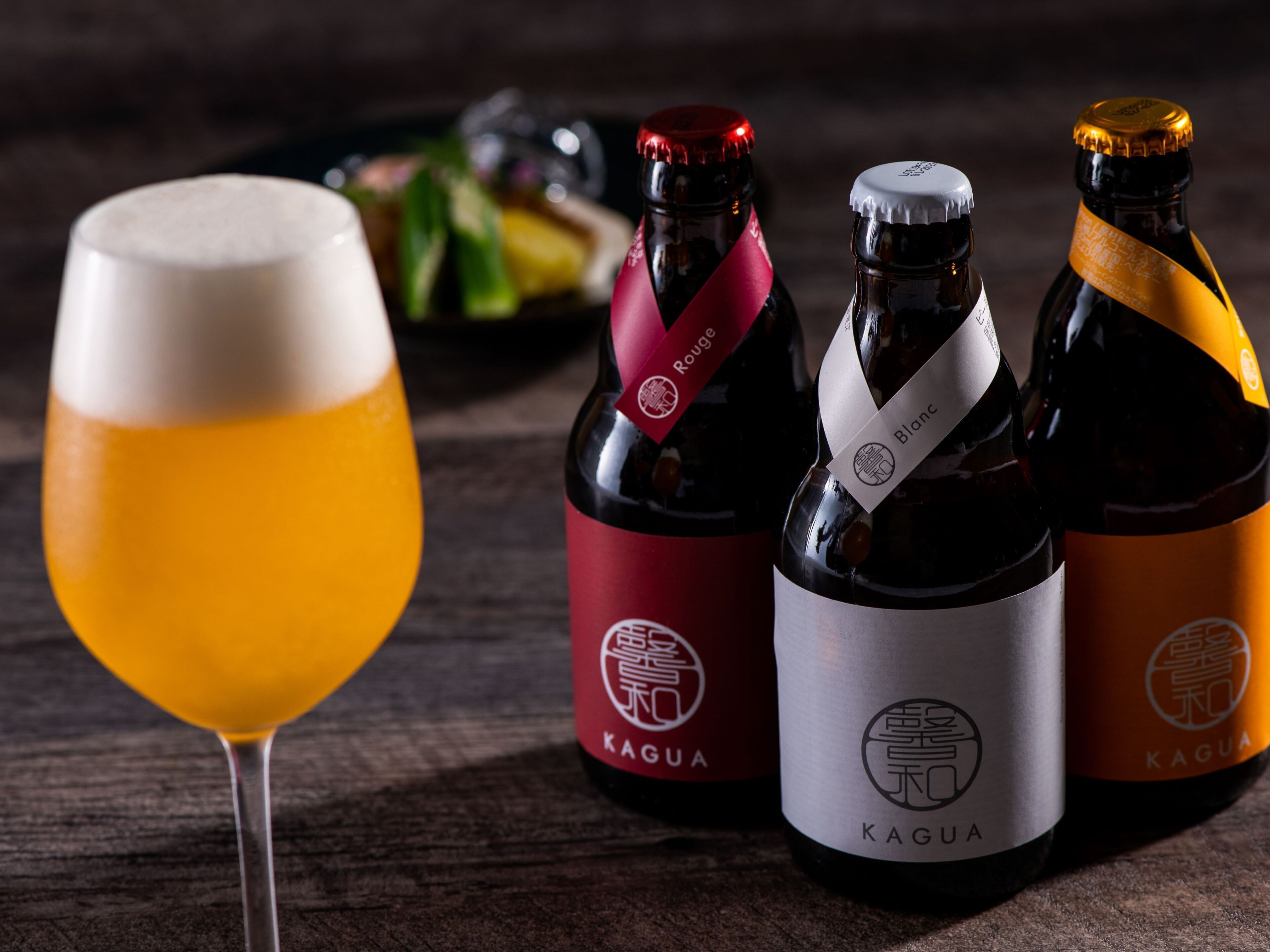 Three bottles of Kagua wine and a glass of beer on a wooden table.