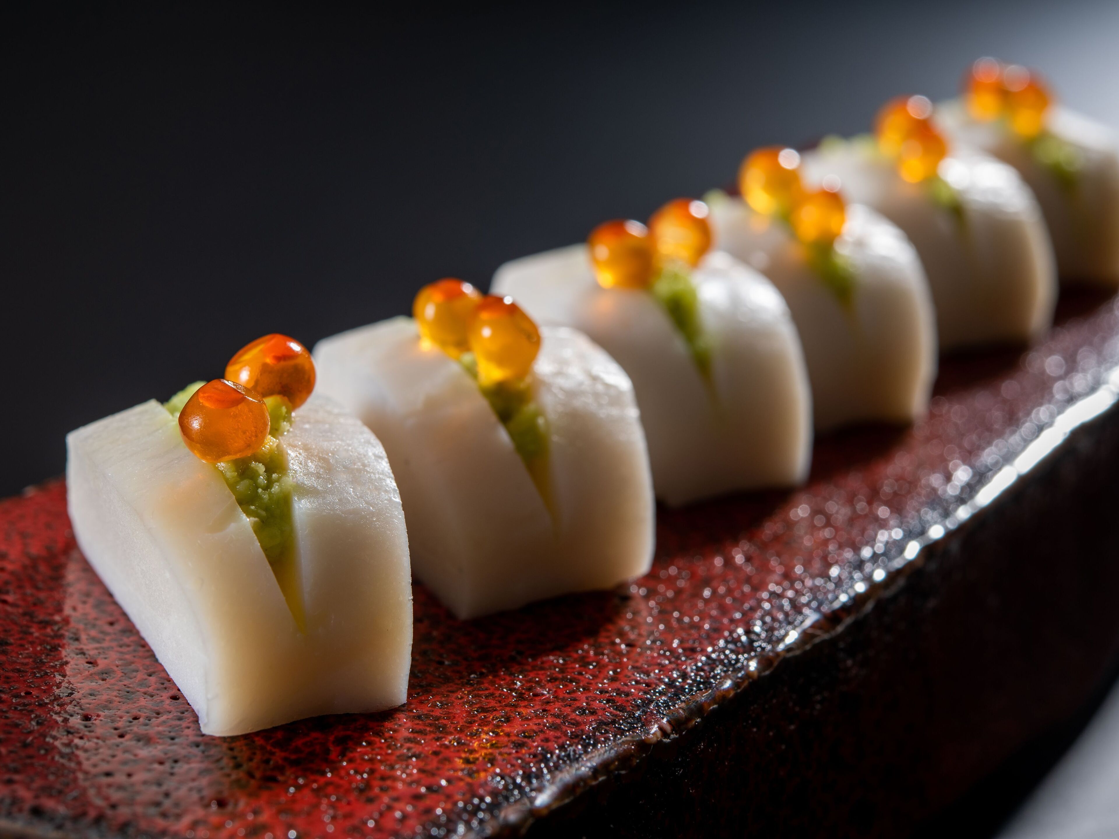 Un plato de sushi con pescado blanco y guarnición verde, servido en un plato rojo con textura.