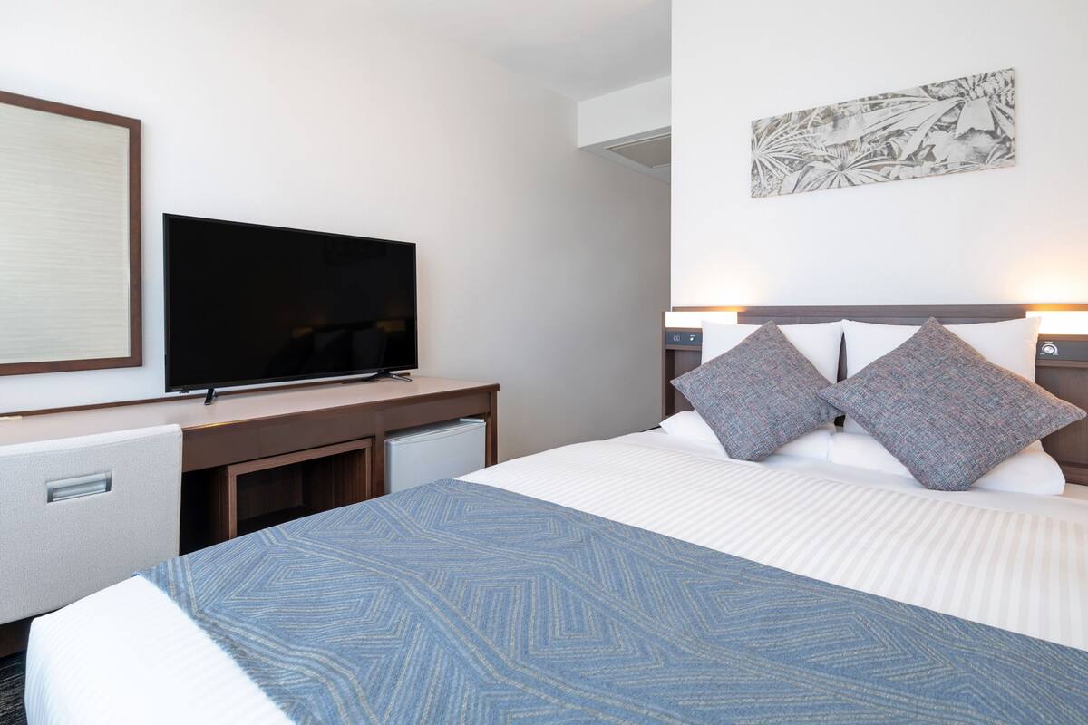 A hotel room with a bed, a flat-screen TV, a desk with a chair, and a wall-mounted artwork.
