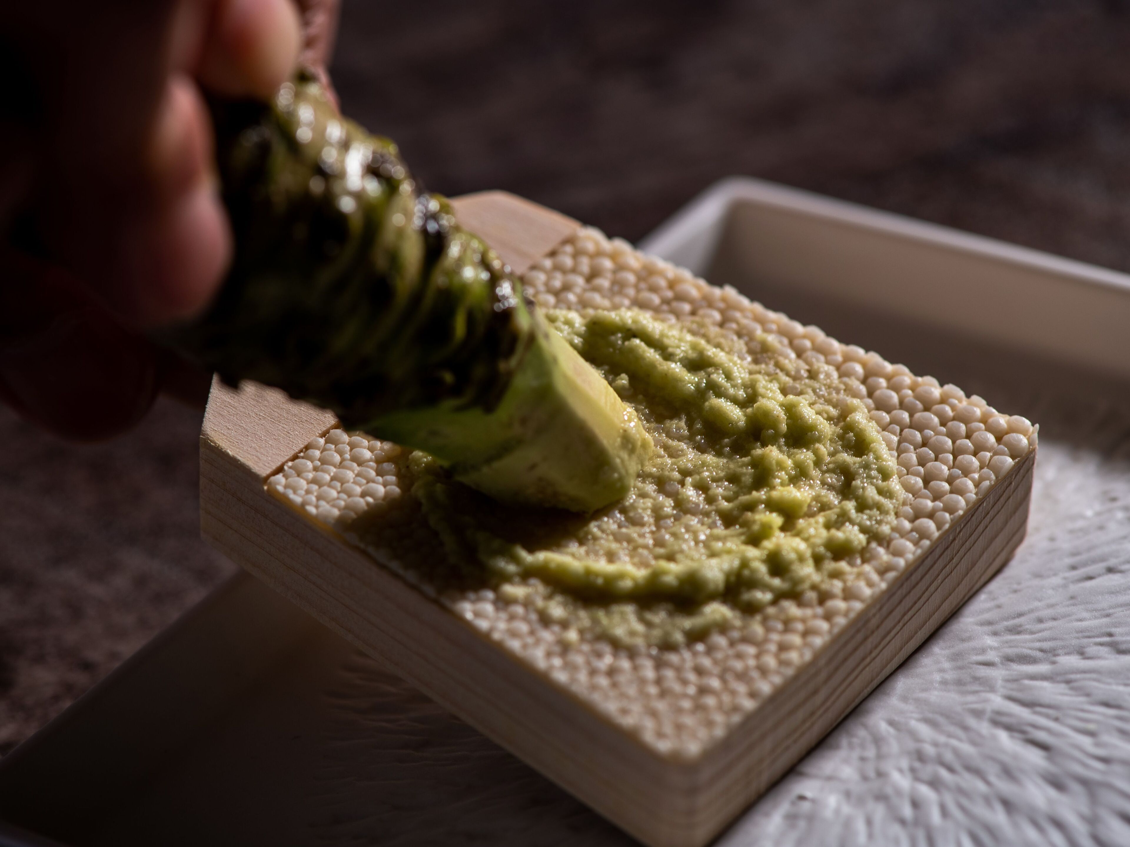 A close-up of a hand spreading a green substance on a textured surface.