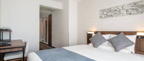 A hotel room with a bed, a desk, and a chair. There is a door leading to another room.
