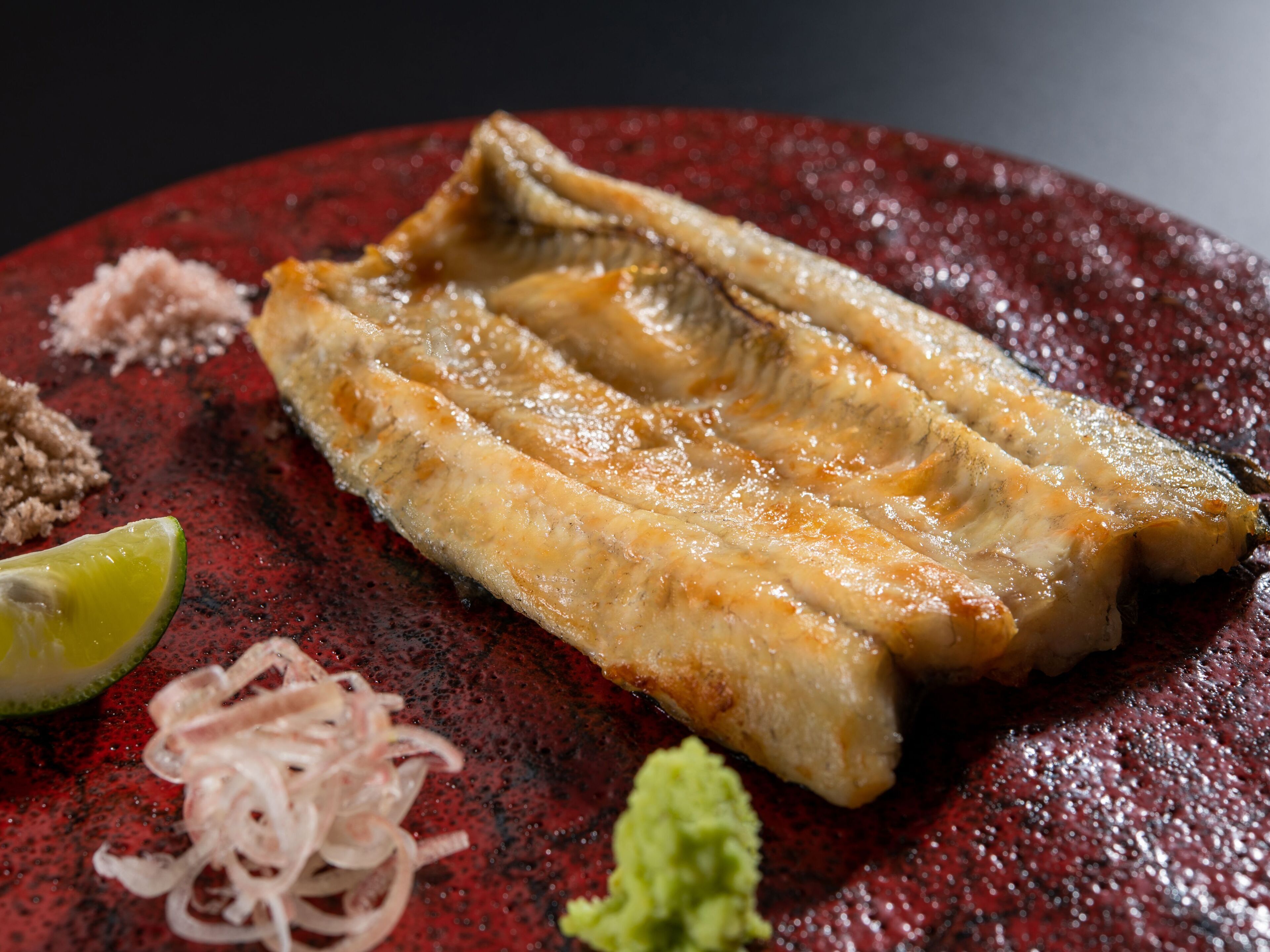 Un plato con un filete de pescado, lima, cebollas encurtidas y una guarnición verde.