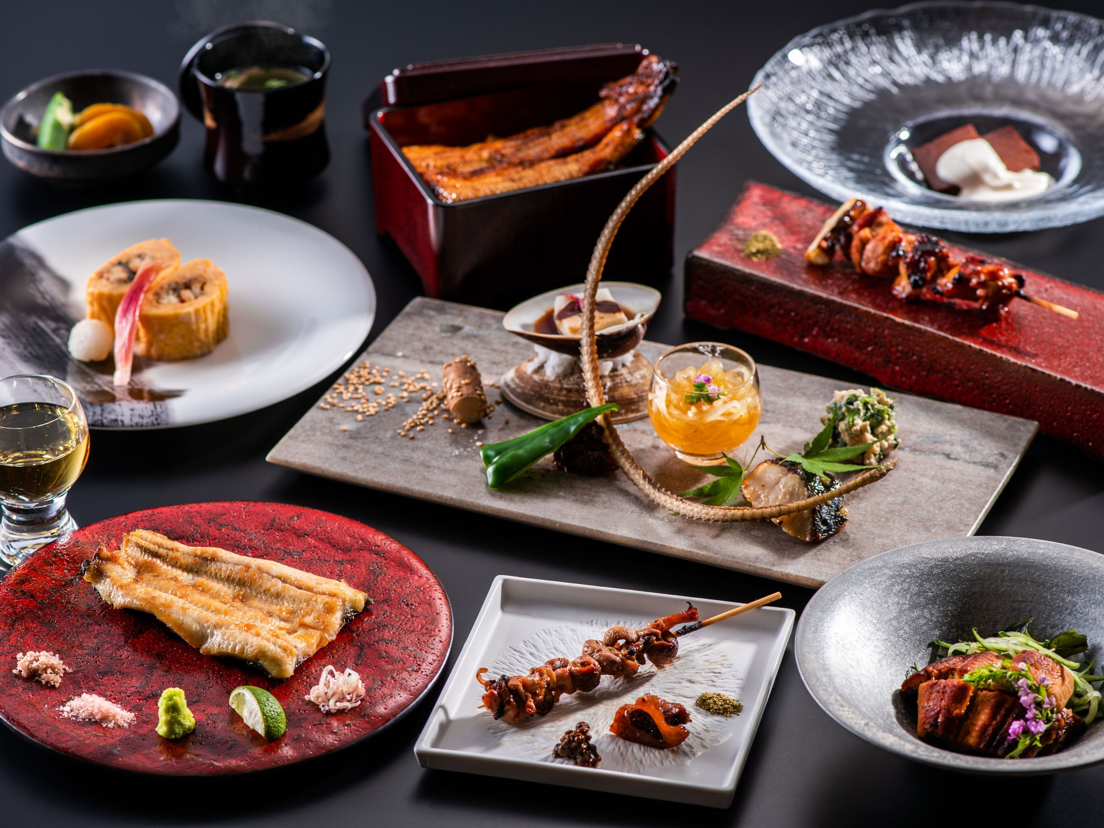 A variety of dishes on a table, including skewers, sashimi, and a bowl of soup.