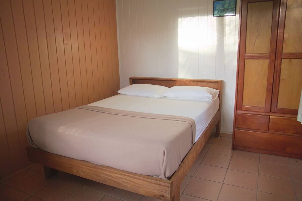 A single bed with a wooden frame and white bedding in a room with wooden paneling and a tiled floor.