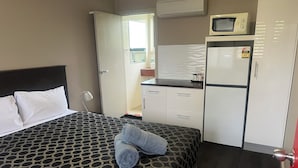 A hotel room with a bed, a desk, a microwave, and a refrigerator.