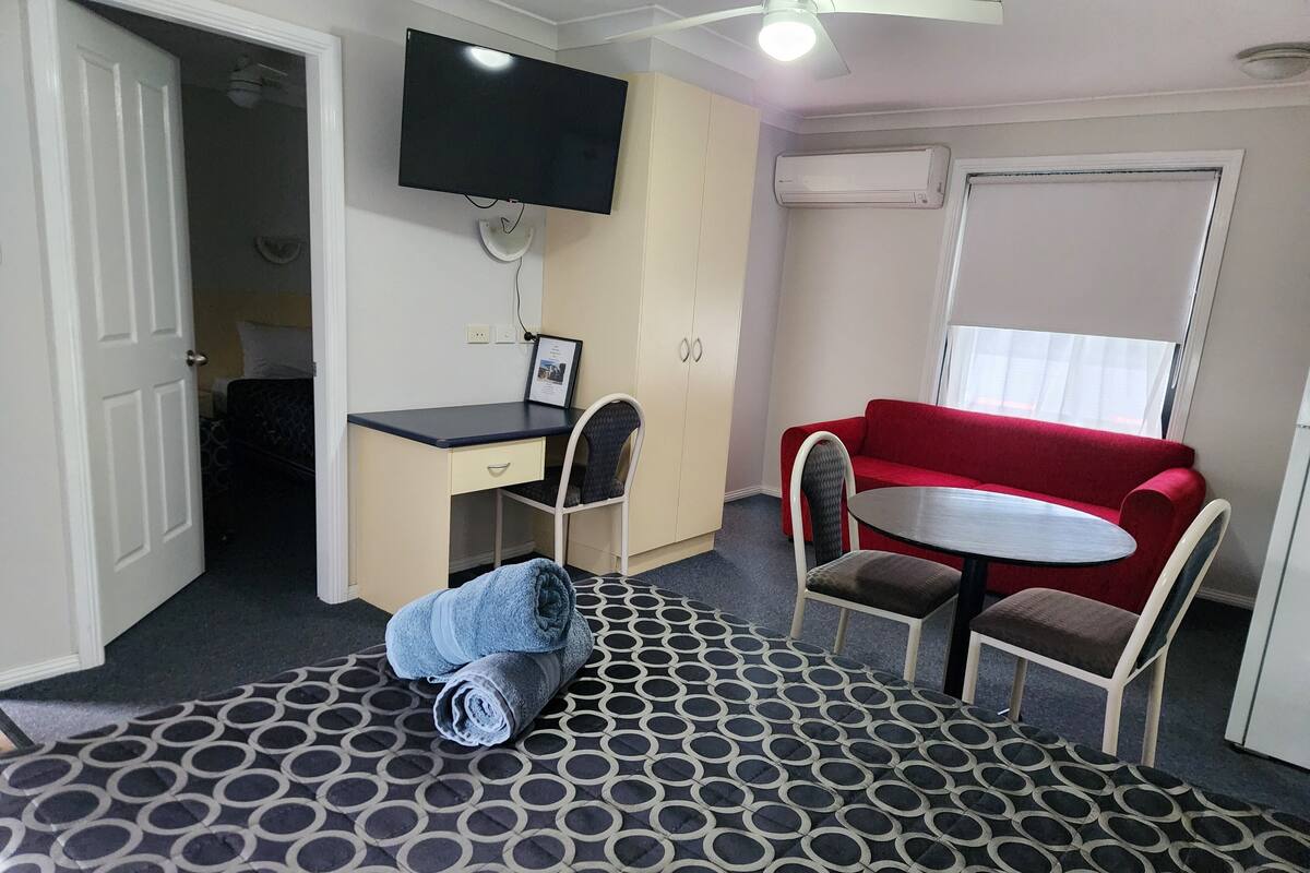 Ein gemütliches Zimmer mit Bett, Schreibtisch, einem roten Schlafsofa und einem an der Wand befestigten Fernseher.