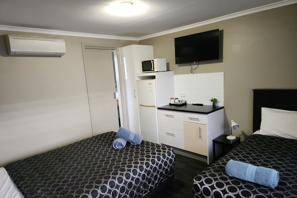 Ein Hotelzimmer mit zwei Betten, einer Küchenzeile, einem Flachbildfernseher und einem Deckenventilator.