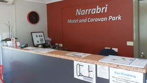 A reception desk at Narrabri Motel and Caravan Park with a clock, Visa and Mastercard logos, and a car washing sign.