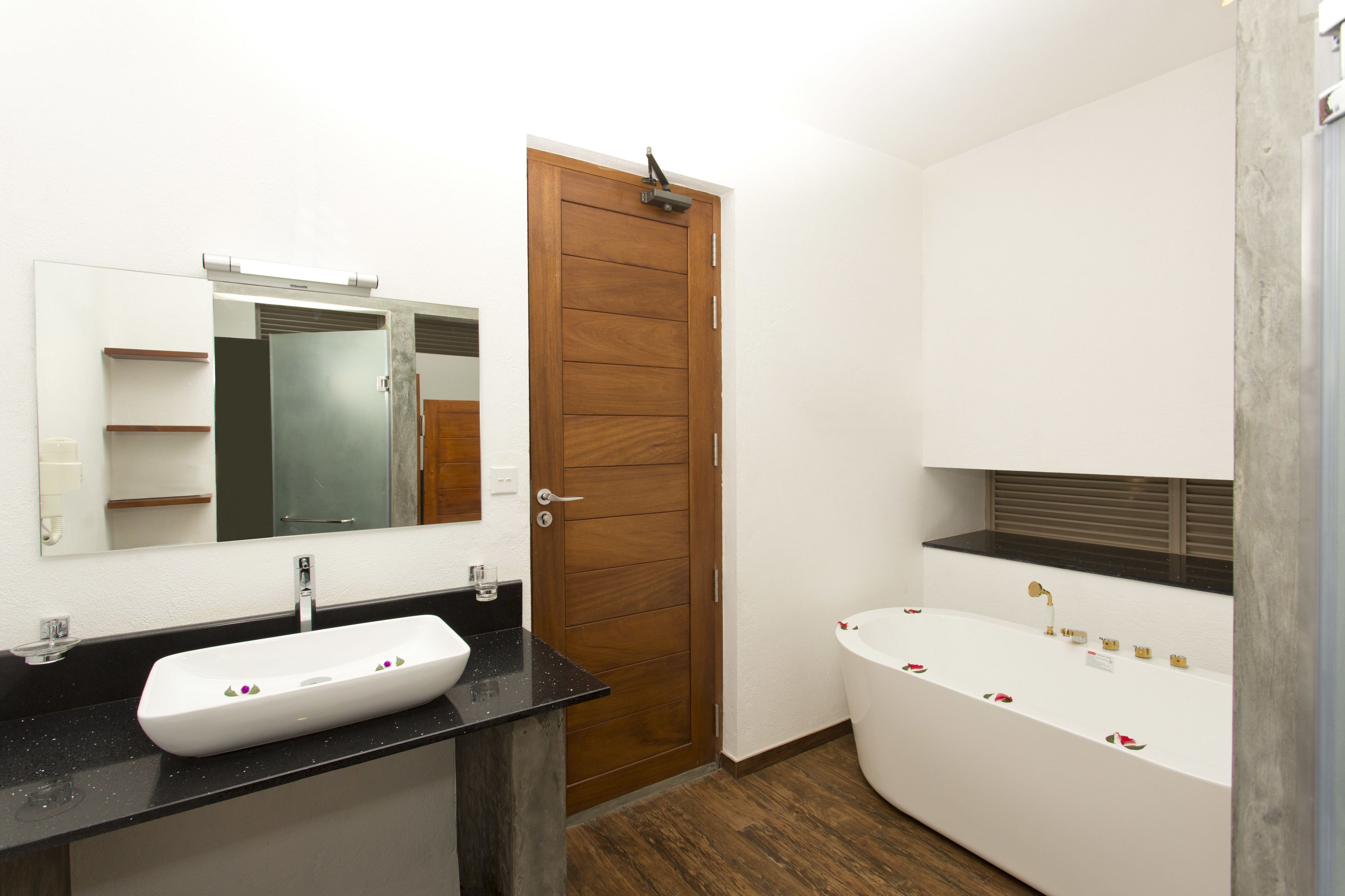 A bathroom with a wooden door, a white sink with a black countertop, and a freestanding bathtub with decorative flowers.