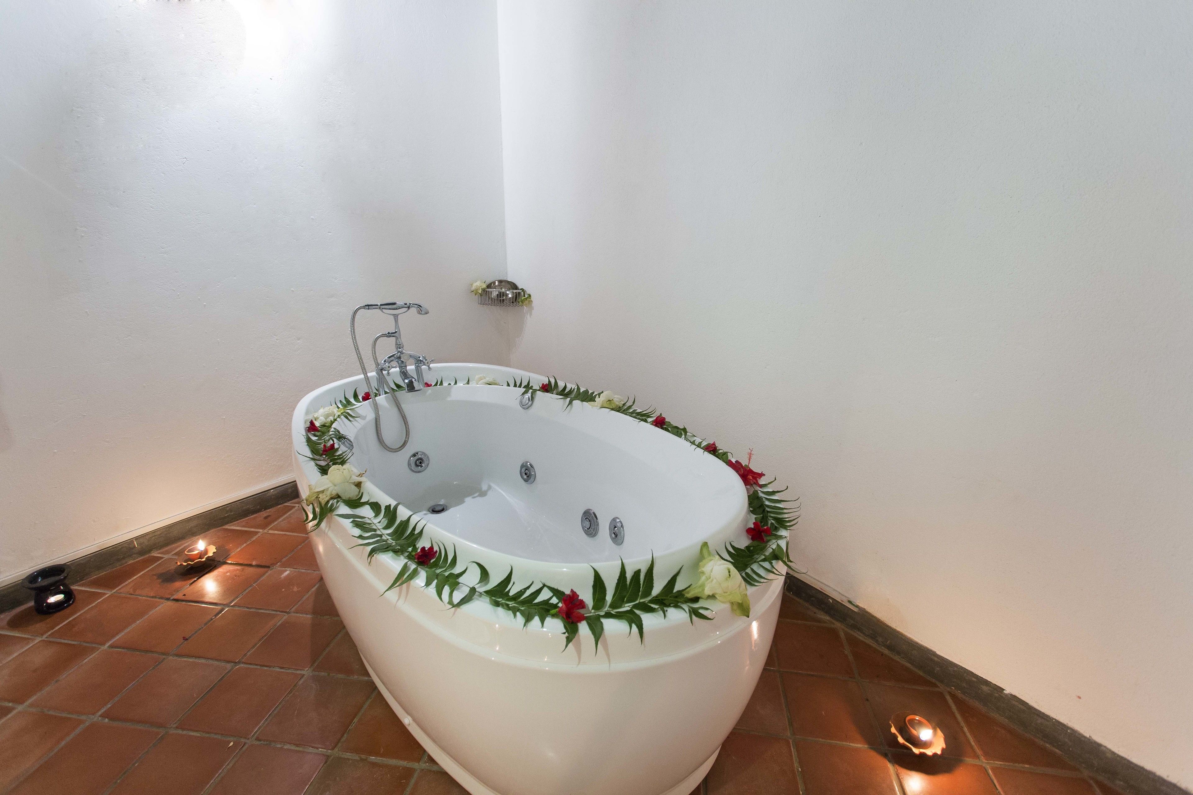 Uma banheira grande e independente com uma guirlanda decorativa, um pequeno prateleira com flores e uma vela acesa no chão.
