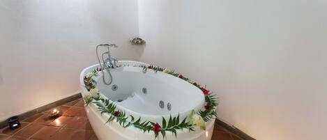 A large freestanding bathtub with a decorative wreath, a small shelf with flowers, and a lit candle on the floor.