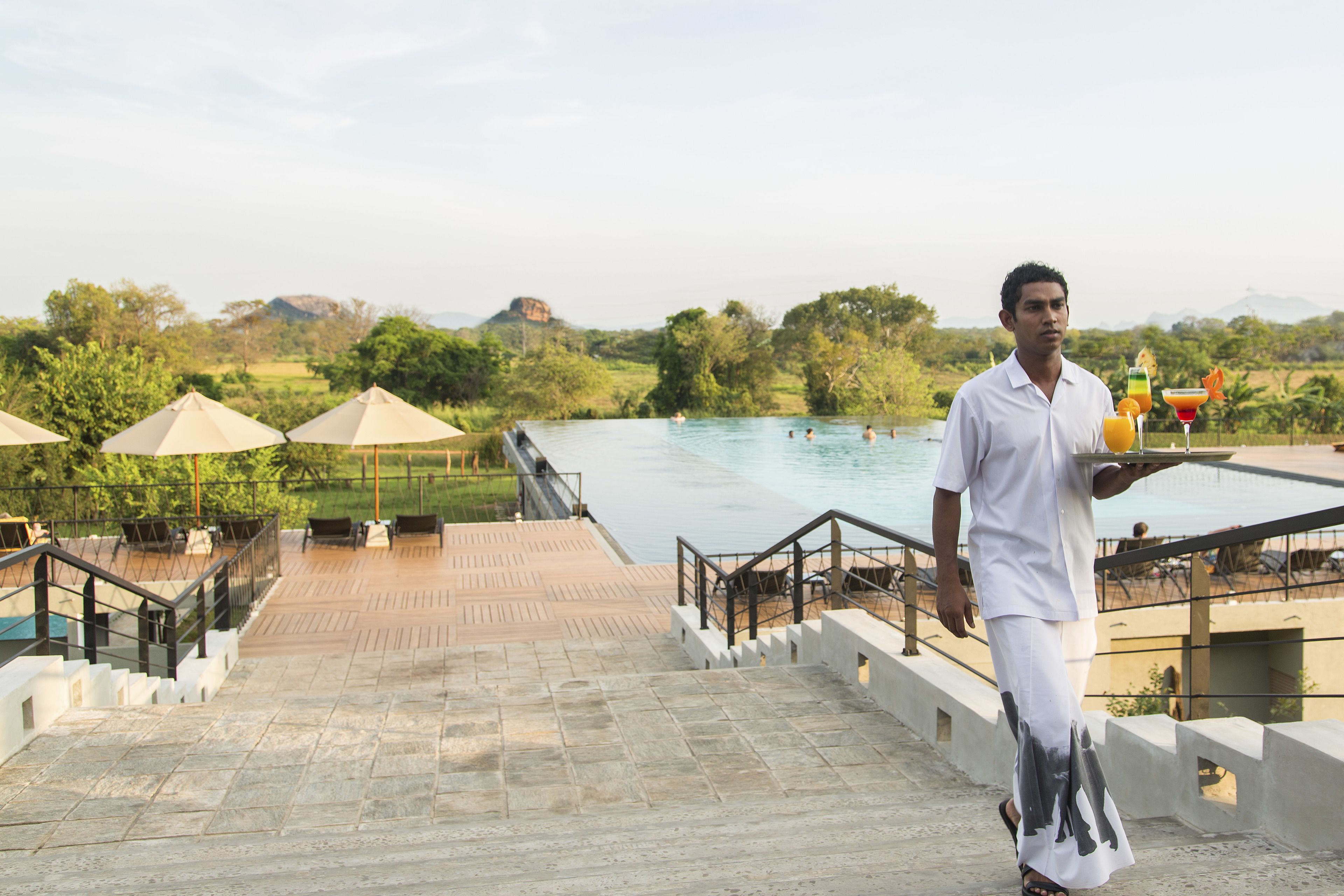 A man in traditional attire walking towards a pool area with steps and umbrellas.