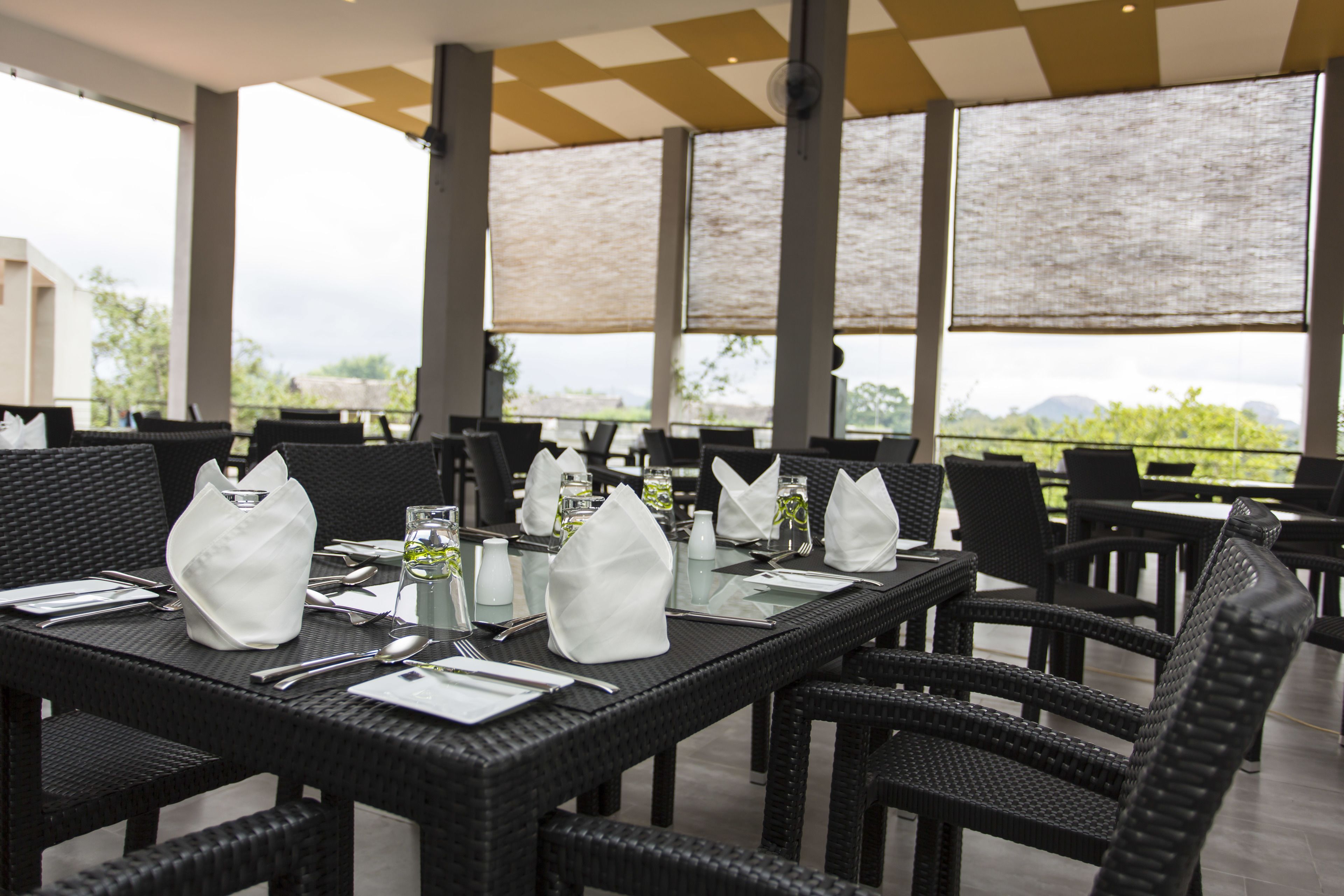 Un restaurante con terraza, mesas dispuestas con servilletas blancas, cubiertos y vasos transparentes.