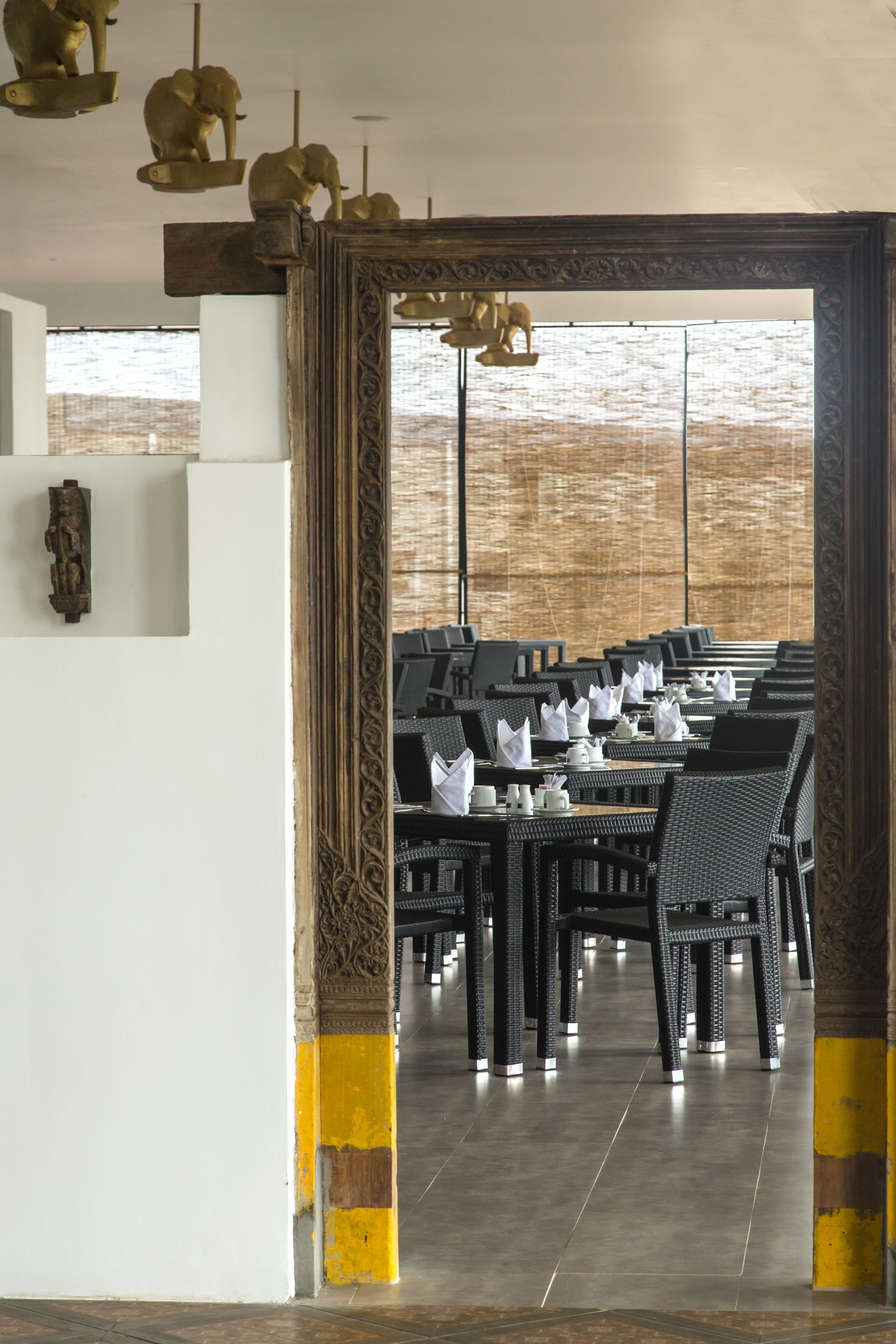 A restaurant with a long table set for dining, a large ornate mirror, and a view through a window.
