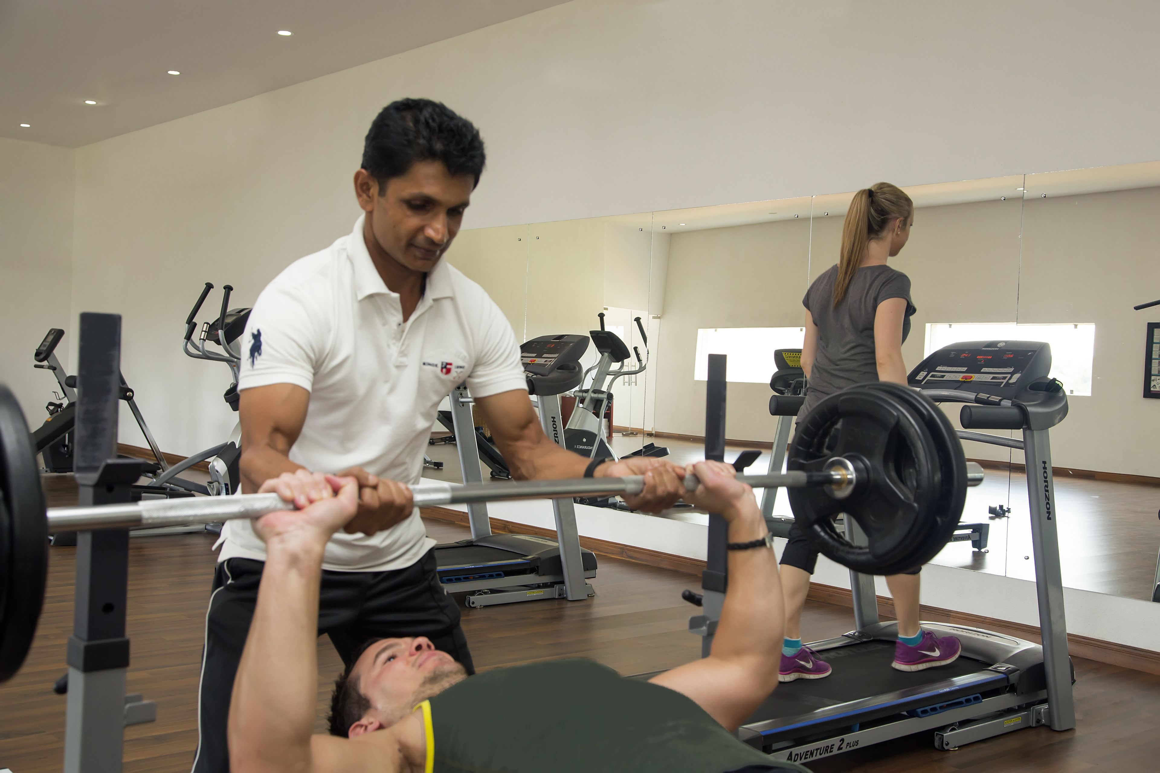 A gym with exercise equipment, a treadmill, and a mirror wall.