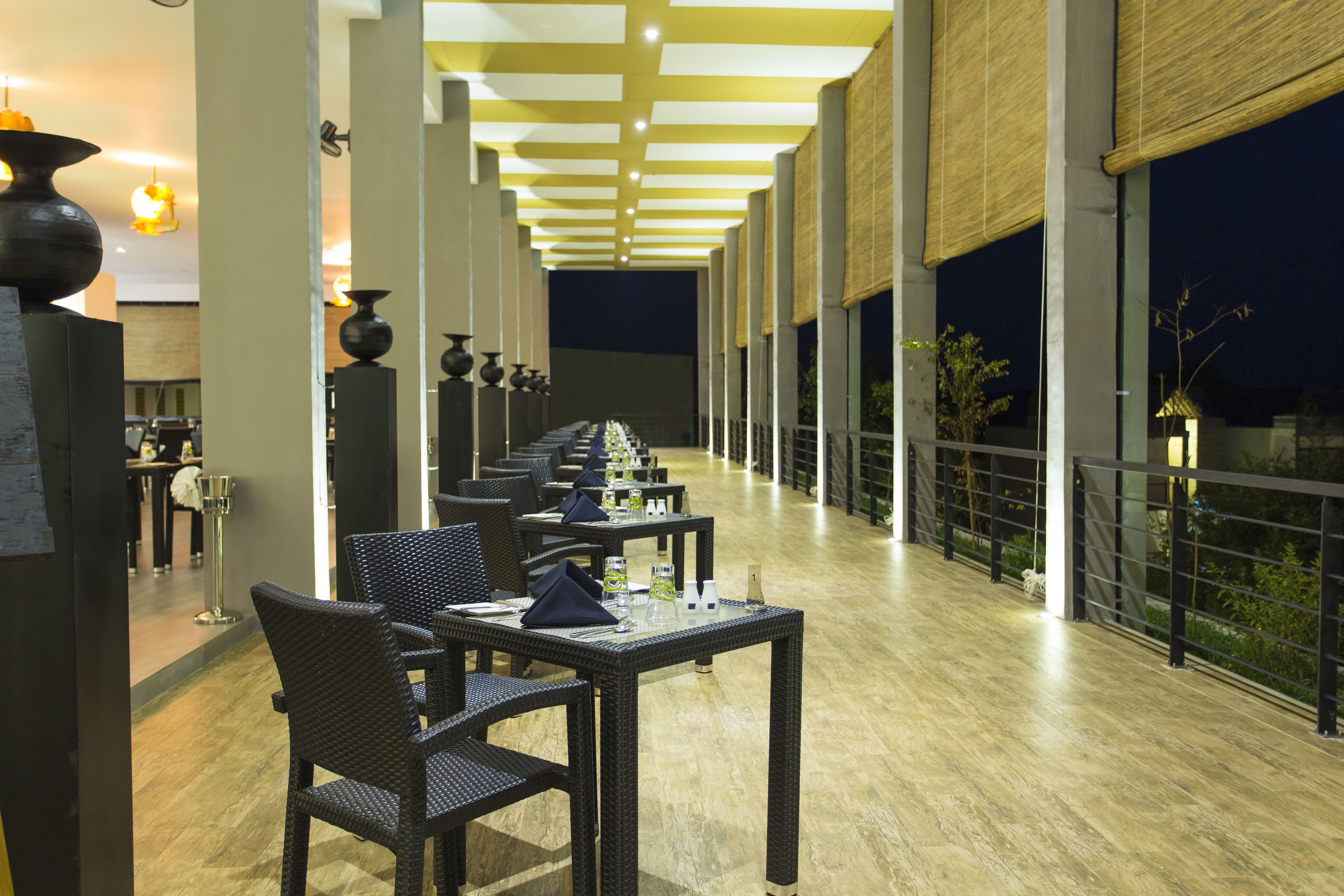 Une grande salle à manger avec des tables et des chaises, un plafond haut avec des luminaires et de grandes fenêtres sur un des murs.