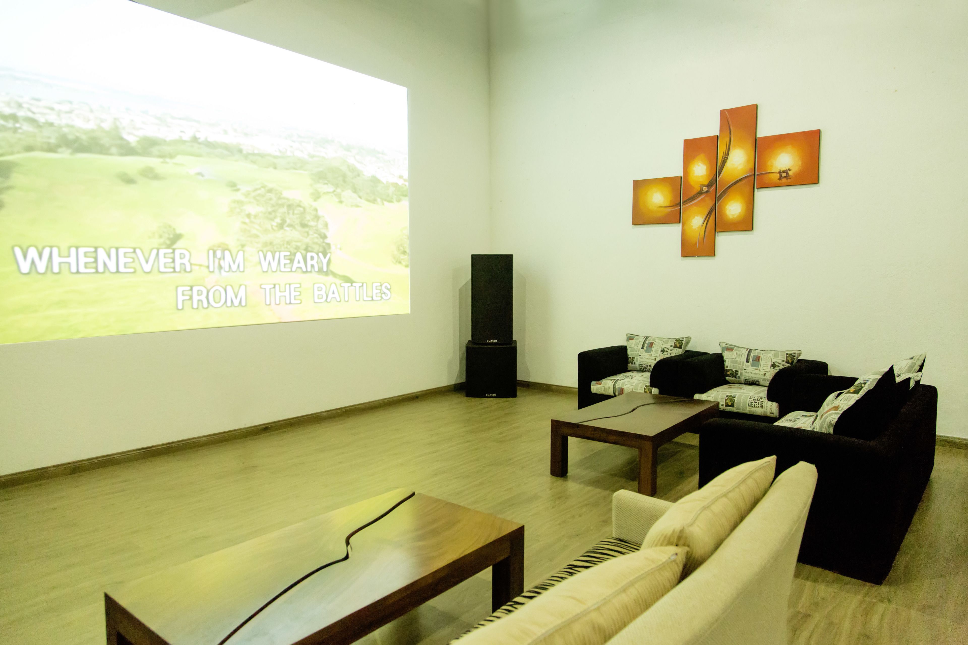 A modern living room with a projector screen displaying a landscape image, a cross-shaped light fixture, and a sofa with patterned cushions.