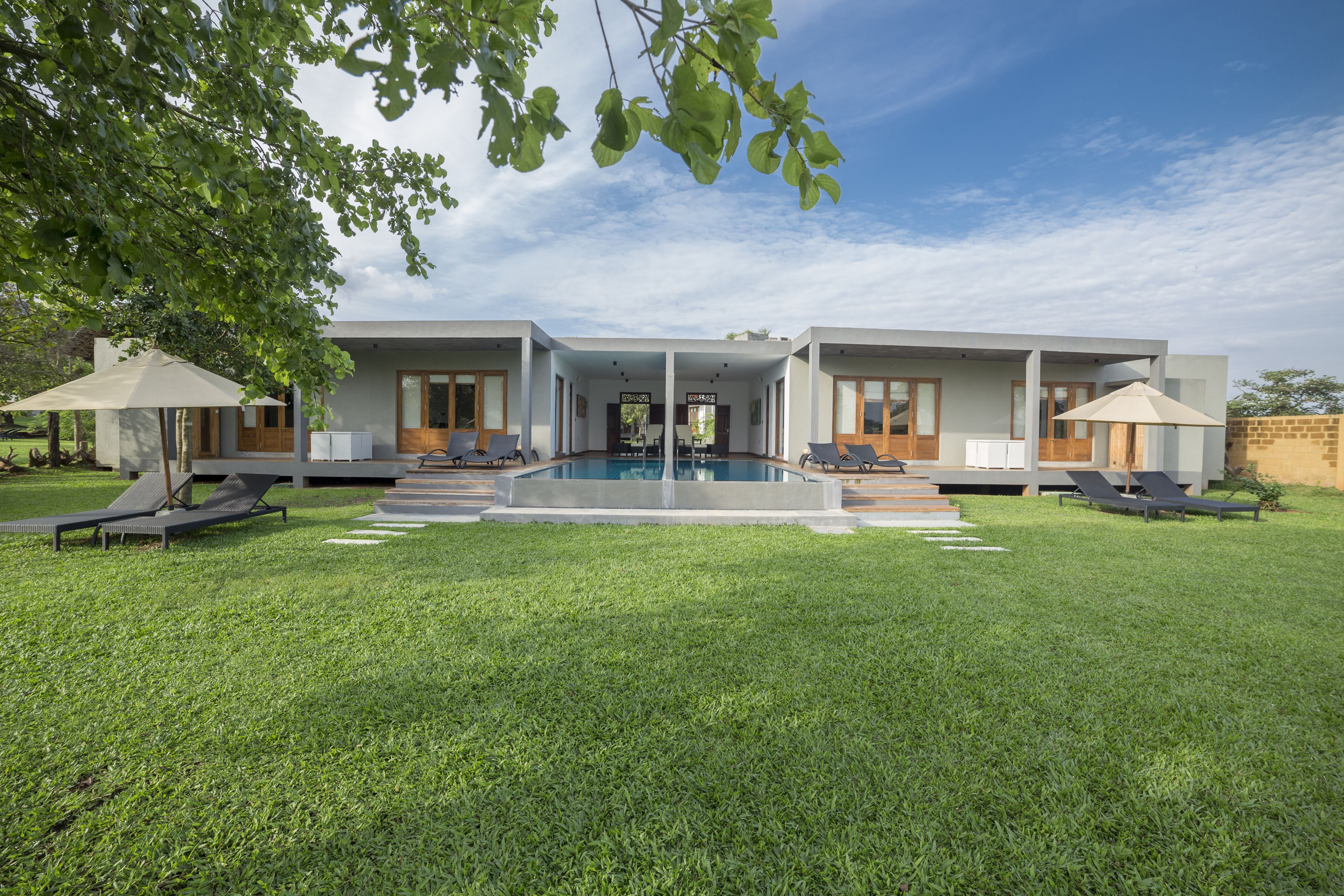 Une maison moderne dotée d’une piscine, de deux chaises longues et d’un patio couvert.