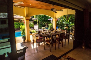 An outdoor dining area with a pool view, wooden tables, and chairs.