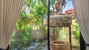 A room with a view of a garden, a thatched structure, and a brick-built circular feature. - Coconut Paradise Villas (Rawai)